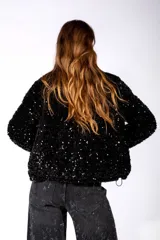 Campera negra con acabado brillante de lentejuelas, cuello alto, cierre frontal y bolsillos laterales con detalles en terciopelo.