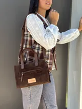 Cartera bandolera de cuero color marrón chocolate, con forro de tela y herrajes dorados. Tiene doble asa de mano y correa larga regulable y desmontable. Incluye bolsillo frontal con cierre y bolsillo interno.