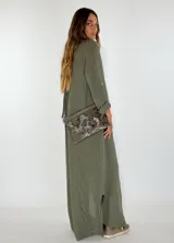 Vestido largo tipo camisero de color verde oliva, con cuello clásico, cierre frontal completo con botones y mangas largas con opción de arremangar. Presenta un corte holgado y fluido.