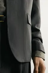 Blazer relaxed fit de color negro, confeccionada en tejido fluido con mezcla de viscosa y lino. Presenta cuello sin solapas, manga larga, bolsillos de solapa en la cadera y cierre frontal de un botón.