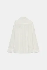 Camisa fluida de corte oversize confeccionada en mezcla de viscosa, con diseño de rayas verticales finas en tono beige sobre fondo blanco. Presenta cuello solapa, cierre frontal con botones, manga larga con puños y un bolsillo de plastrón en el pecho.