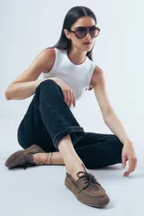 Mocasín de estilo náutico confeccionado en cuero gamuzado color tostado, con cordones decorativos laterales y en el empeine.