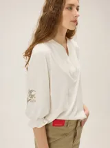 Remera de algodón de color negro con cuello en V y mangas tres cuartos abullonadas, con puños elásticos y detalles de bordado artesanal en las mangas.