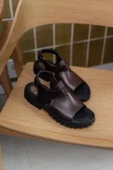 Sandalias de cuero con textura grabada, diseño de punta abierta y talón descubierto con tira ajustable. Poseen una suela de plataforma dentada en tono tierra.