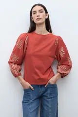 Remera de color crudo con mangas largas abullonadas, decoradas con bordados en color negro. Presenta un diseño de cuello redondo y corte recto.