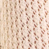 Cardigan de punto fantasía color crudo, con mangas largas y cierre delantero con tiras para atar. Presenta detalles de terminación en color negro en el ruedo y los puños.