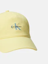 Gorra de béisbol de algodón color amarillo pálido, con visera curva y bordado frontal del logo de Calvin Klein en azul claro.