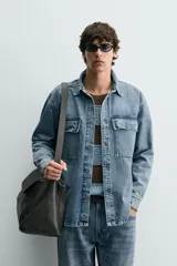 Sobrecamisa de denim de algodón con efecto lavado, corte regular fit, cuello solapa, cierre frontal de botones, manga larga con puños abotonados y dos bolsillos frontales con solapa en el pecho.