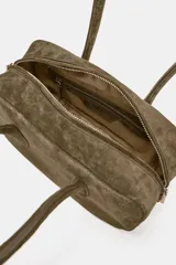 Bolso de hombro de formato alargado confeccionado en gamuza color marrón. Cuenta con doble asa de hombro y cierre superior mediante cremallera metálica.