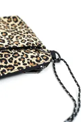 Bandolera pequeña con estampado animal print de leopardo, bolsillos frontales con cierre y correa ajustable de cordón negro con detalles blancos.