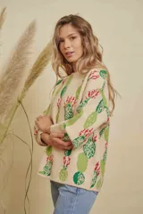 Buzo tejido de punto con diseño estampado de cactus en tonos verdes y rojos sobre base color crema. Presenta cuello redondo y mangas largas con puños acanalados.
