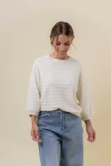 Buzo de tejido liviano color crema, con diseño de textura calada y líneas horizontales. Presenta cuello redondo, mangas largas levemente abullonadas y terminaciones en rib.