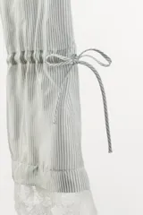 Pantalón capri de tiro medio con cintura elástica, confeccionado en tejido de viscosa con estampado de rayas verticales. Presenta un diseño de bajo ajustable mediante lazadas laterales y detalle de encaje en el ruedo.