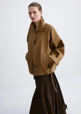 Chaqueta corta de algodón color marrón tostado, con cuello alto, cierre frontal de botones, bolsillos ribeteados y mangas largas con trabillas ajustables en los puños.