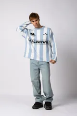Sweater de tejido de punto con diseño a rayas verticales en color celeste y blanco. Presenta un corte holgado, cuello redondo y detalles gráficos en negro en el frente, incluyendo la palabra 'Argentina' y estrellas bordadas.