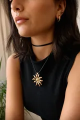 Collar con dije de acero quirúrgico en forma de flor tipo margarita, montado sobre un tiento de cuero negro.