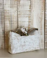 Cartera de hombro color beige con textura tipo cocodrilo, confeccionada en gamuza. Presenta un diseño estructurado con una cadena metálica decorativa en la parte superior del asa y cierre principal.