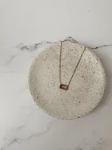 Collar de cadena fina dorada con un dije rectangular que contiene una piedra de cristal en tono rosado.