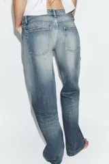 Jeans de tiro bajo y cinco bolsillos, con diseño de pierna ancha y larga. Presenta roturas y desgastes sutiles en la parte delantera. Cierre frontal con cremallera y botón metálico.