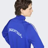 Campera deportiva Adidas de la Selección Argentina, color azul con las icónicas tres tiras blancas en las mangas. Presenta cuello alto, cierre frontal, logo del Trifolio bordado en el pecho y escudo de la AFA.