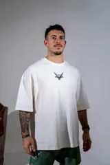 Remera de corte oversize color blanco, con cuello redondo y mangas cortas. Presenta un pequeño estampado gráfico central en el pecho con diseño de querubín con alas.