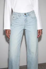Jeans de mezclilla en color negro gastado, tiro bajo, corte de pernera recta y diseño clásico de cinco bolsillos con cierre frontal de cremallera y botón metálico.