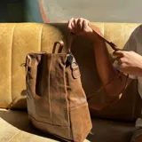 Mochila urbana de eco-cuero marrón tostado, de diseño estructurado con bolsillos laterales y asa superior.