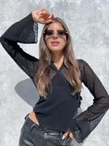 Remera de encaje negro con diseño cruzado frontal y lazo lateral para ajustar. Presenta mangas largas con terminación acampanada y un delicado patrón de pequeñas flores bordadas en toda la prenda.