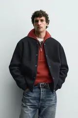 Chaqueta relaxed fit de color negro, confeccionada en tejido de canalé con mezcla de lana. Presenta cuello redondo, puños y dobladillo en rib elástico, bolsillos frontales de vivo y cierre con botones a presión.