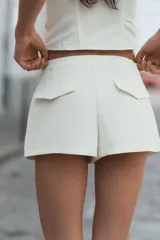 Short mini de tiro bajo color blanco con aplicación de botones dorados frontales y cierre lateral con cremallera oculta.