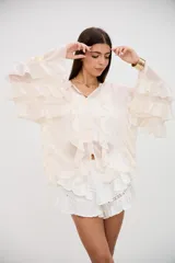 Blusa color crudo con volados en el frente y en las mangas largas, confeccionada en tela semitransparente con cierre frontal de botones.