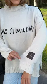 Sweater oversized crudo de tejido de punto, con hombros caídos y mangas largas. Presenta líneas negras en contraste en los hombros, bordado artesanal con la frase "e pur si muove" en el frente y aberturas laterales en el dobladillo.