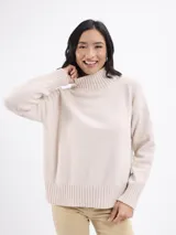 Buzo de punto color beige, con cuello alto y mangas largas con puños acanalados.