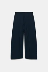 Pantalón de tiro medio de corte wide leg, confeccionado en mezcla de lyocell con patrón de rayas diplomáticas. Presenta bolsillos laterales ocultos, pliegues delanteros marcados y cierre frontal con cremallera, botón y ganchos metálicos.
