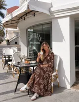 Vestido largo holgado de color marrón chocolate, con estampado geométrico y floral en tono crudo. Cuenta con cierre frontal de botones, cuello camisero y mangas tres cuartos.