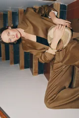 Bolso mini de formato redondeado con acabado metalizado dorado y textura acanalada. Presenta un asa de mano rígida metálica y cierre superior mediante cremallera.