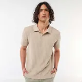 Remera de punto calado color beige, de manga corta, con cuello polo y escote en V sin botones.