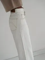 Pantalón vaquero de tiro alto y corte recto, color blanco, con aberturas laterales en los bajos y detalles de terminación en cuero.