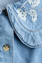 Blusa corta de denim de algodón con cuello Peter Pan bordado, mangas cortas abullonadas y cierre frontal con botones.