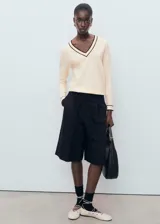 Jersey de punto fino en color crema con cuello de pico y detalles en contraste color marrón en el cuello y los puños. Presenta un diseño recto de manga larga.