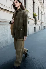 Chaqueta de algodón encerado con diseño de cuadros en tonos verde oliva, beige y líneas rojas. Presenta cuello solapa, cierre frontal con botones a presión metálicos, bolsillos de plastrón con solapa y un detalle de pañuelo desmontable sobre los hombros.