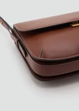 Bolso de hombro tipo bandolera en color marrón, con diseño estructurado de solapa, cierre metálico a presión y costuras decorativas en contraste. Incluye correa larga ajustable.