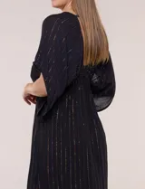 Vestido largo negro confeccionado en gasa con hilos de lurex en relieve vertical. Presenta escote en V profundo con lazo frontal y borlas, mangas holgadas tipo kimono, cintura elastizada y falda fluida con ruedo con volante.