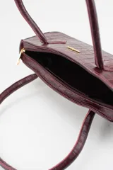 Cartera tipo baguette color negro con textura efecto cocodrilo, diseño alargado, doble asa de mano y cierre superior.