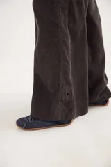 Pantalón sastrero de tiro medio confeccionado en pana de algodón. Presenta un diseño de pierna ancha con costuras verticales decorativas, bolsillos delanteros y traseros, y un detalle de aplique con ojalillo metálico en el ruedo de una de las piernas.