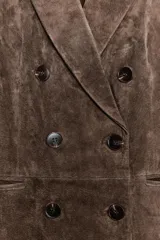 Blazer cruzado de mujer, color marrón oscuro, confeccionado en piel 100%. Presenta cuello solapa, manga larga con hombreras, bolsillos delanteros de doble vivo y cierre frontal cruzado con botones oscuros.