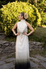 Vestido largo de satén con diseño degradé que transiciona de marfil en la parte superior a verde oscuro y negro en el dobladillo. Presenta cuello halter, diseño superior irregular, cintura elástica y falda larga con aberturas laterales.