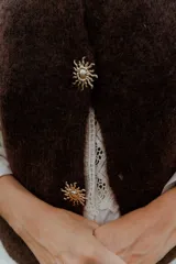 Chaleco de punto en color marrón oscuro, con cuello redondo y cierre frontal mediante botones metálicos decorativos con forma de sol.