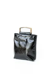 Cartera tipo mini bag de cuero negro con acabado brillante y estructura rígida. Presenta un diseño cuadrado con manijas metálicas doradas integradas en la parte superior.