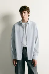 Camisa de corte regular fit confeccionada en tejido de algodón con diseño de rayas verticales finas. Presenta cuello italiano, manga larga con puños abotonados y cierre frontal mediante botonadura.